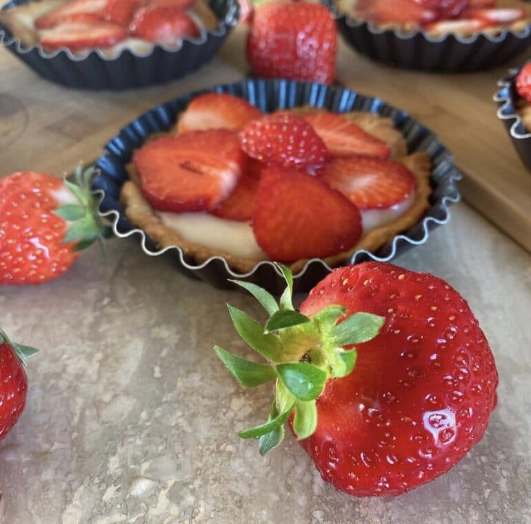 Tarte aux fraises encore dans son moule, joliment décoré de fraises autour.