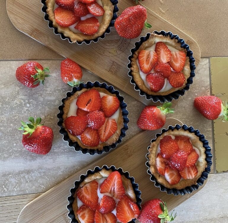 Plusieurs tartes aux fraises présentées sur des planches en bois parsemé de fraises entières.